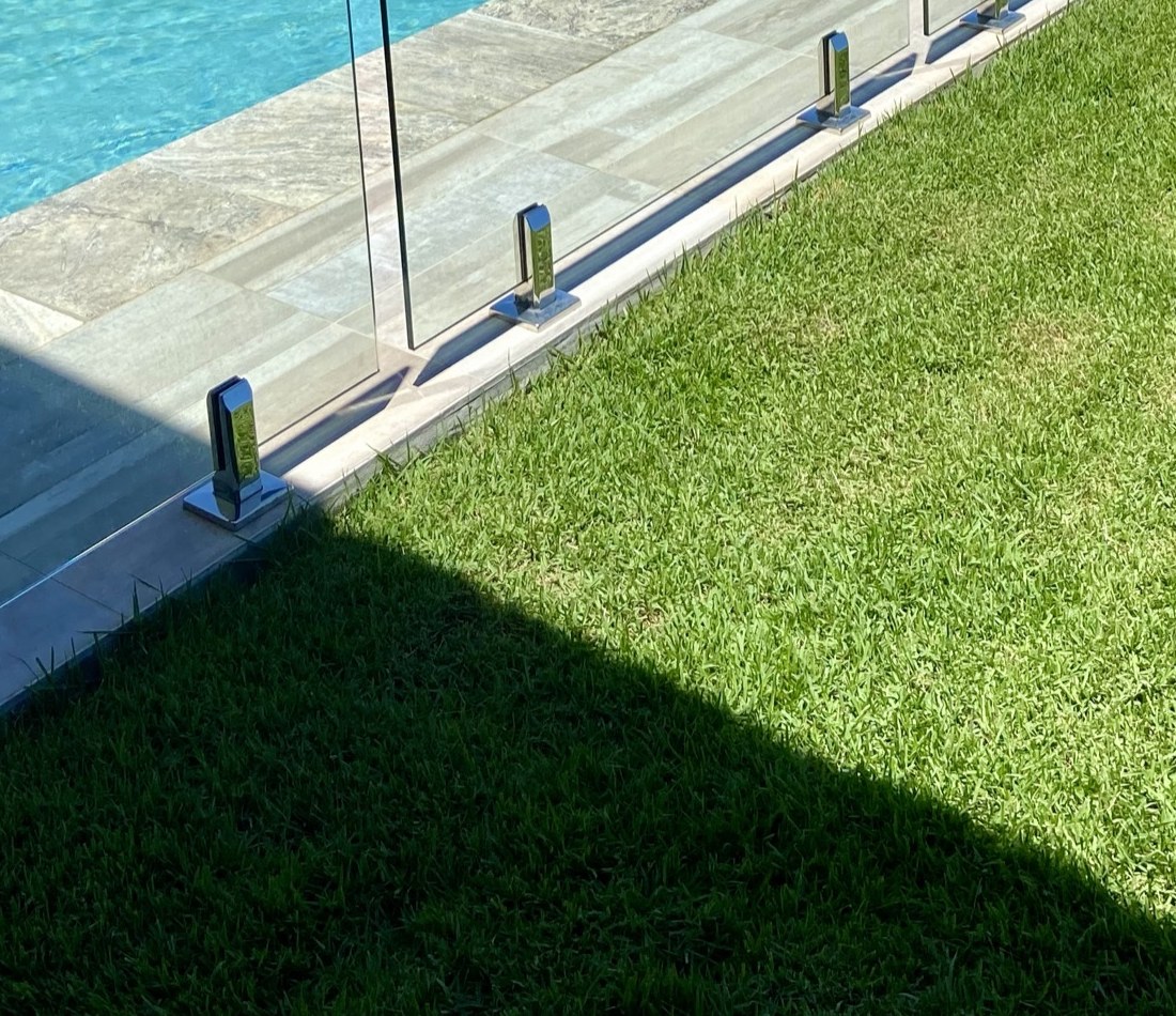 Close-up of frameless glass panel on polished stainless spigots at the pool edge