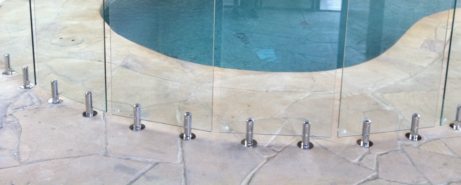 Row of polished stainless steel spigots holding curved frameless glass panels